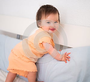 lifestyle home portrait of adorable and beautiful 9 months old baby girl learning to stand up by holding bed frame smiling