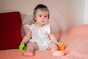 lifestyle home portrait of adorable and beautiful Asian Caucasian mixed baby girl playing on bed with color blocks excited and