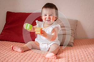 lifestyle home portrait of adorable and beautiful Asian Caucasian mixed baby girl playing on bed with color blocks excited and