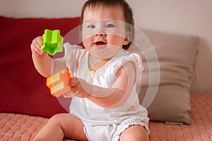 lifestyle home portrait of adorable and beautiful Asian Caucasian mixed baby girl playing on bed with color blocks excited and