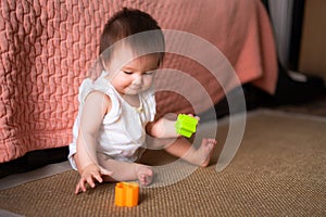lifestyle home portrait of adorable and beautiful Asian Caucasian mixed baby girl playing on the floor with color blocks excited