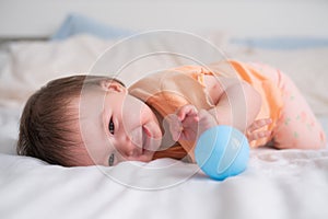 lifestyle home portrait of happy and beautiful 8 months old baby girl mixed race Asian Caucasian playing with ball cheerful on bed