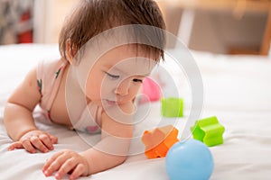 lifestyle home portrait of sweet and adorable mixed ethnicity Asian Caucasian baby girl playing with color blocks on bed excited