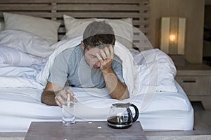 Lifestyle home portrait of young exhausted and wasted man waking up suffering headache and hangover after drinking alcohol at nigh