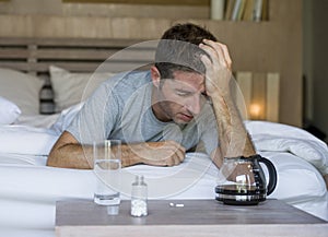 Lifestyle home portrait of young exhausted and wasted man waking up suffering headache and hangover after drinking alcohol at nigh