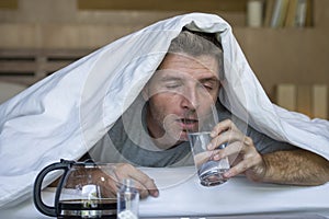 Lifestyle home portrait of young exhausted and wasted man waking up suffering headache and hangover after drinking alcohol at nigh