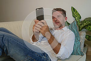 Lifestyle home portrait of young handsome and happy man using mobile phone lying relaxed and cheerful at home sofa couch using int