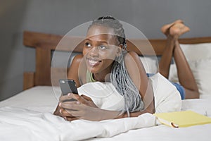 Lifestyle home portrait of young happy and attractive black African American woman lying on bed using social media app in mobile