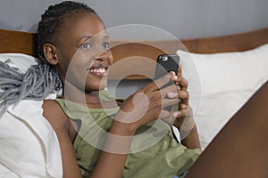 Lifestyle home portrait of young happy and attractive black afro American woman lying on bed using social media app in mobile