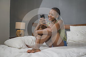 Lifestyle home portrait of young happy and attractive black afro American woman lying on bed using social media app in mobile