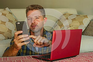 Lifestyle home portrait of young happy and attractive man at home sofa couch working on laptop computer using mobile phone relaxed