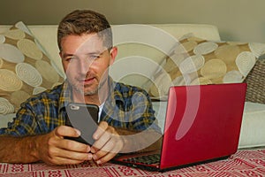 Lifestyle home portrait of young happy and attractive man at home sofa couch working on laptop computer using mobile phone relaxed