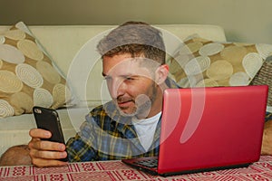 Lifestyle home portrait of young happy and attractive man at home sofa couch working on laptop computer using mobile phone relaxed