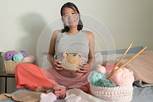 Lifestyle home portrait of young happy and beautiful Asian Chinese woman knitting little bonnet for the new baby relaxed in her