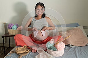 Lifestyle home portrait of young happy and beautiful Asian Chinese woman knitting little bonnet for the new baby relaxed in her