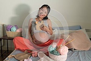 Lifestyle home portrait of young happy and beautiful Asian Japanese woman knitting little bonnet for the new baby relaxed in her