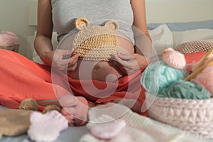 Lifestyle home portrait of young happy woman knitting showing little bonnet for the new baby relaxed in her bedroom in maternity