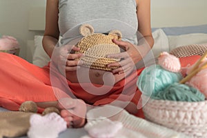 Lifestyle home portrait of young happy woman knitting showing little bonnet for the new baby relaxed in her bedroom in maternity