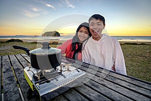 Lifestyle image of young happy asian couple eating hot pot stove on a table outdoor along beach. Leisure activity image of chinese