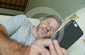 Lifestyle indoors portrait of young happy and attractive man at home sofa couch using internet social media app on mobile phone ne