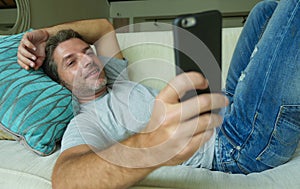 Lifestyle indoors portrait of young happy and attractive man at home sofa couch using internet social media app on mobile phone ne
