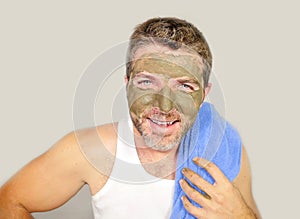 Lifestyle isolated portrait of young attractive and happy man with bathroom towel smiling with green cream on his face applying f