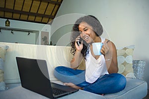 Lifestyle isolated portrait of young happy and gorgeous black afro American woman talking on mobile phone while working on laptop