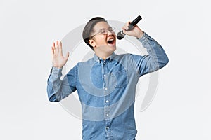 Lifestyle, leisure and people concept. Carefree asian guy in glasses and braces singing song at karaoke bar, holding