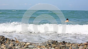 Lifestyle man walks into the sea on a pebble beach and swims on the wave.