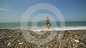 Lifestyle man walks into the sea on a pebble beach and swims on the wave.