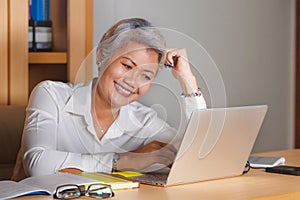 Lifestyle office portrait of attractive and happy successful middle aged Asian woman working at laptop computer desk smiling