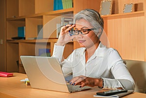 Lifestyle office portrait of attractive and happy successful middle aged Asian woman working at laptop computer desk smiling