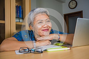 Lifestyle office portrait of attractive and happy successful middle aged Asian woman working at laptop computer desk smiling