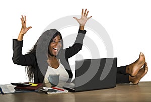 Happy and attractive black afro American businesswoman working excited with feet on computer desk smiling relaxed celebrating busi