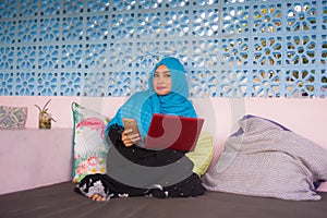 Young beautiful and happy woman in muslim hijab head scarf working with laptop computer and mobile phone networking running inter