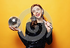 Lifestyle, party and people concept - woman in evening dress holding microphone and disco ball