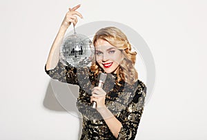 Lifestyle, party and people concept - woman in evening dress holding microphone and disco ball