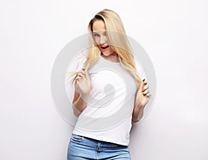 Lifestyle and people concept - Beautiful happy blond girl touches her hair. Casual clothes. White background.