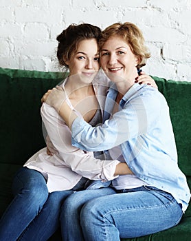 Lifestyle and people concept - Beautiful senior mom and her adult daughter are hugging, looking at camera and smiling.