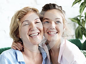 Lifestyle and people concept - beautiful senior mom and her adult daughter are hugging, looking at camera and smiling.