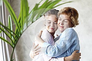 Lifestyle and people concept - Beautiful senior mom and her adult daughter are hugging, looking at camera and smiling.