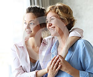 Lifestyle and people concept - Beautiful senior mom and her adult daughter are hugging, looking at camera and smiling.