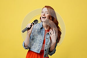 Lifestyle and People Concept: Expressive beauty ginger hair model girl in casual jean cloth singer with a microphone.