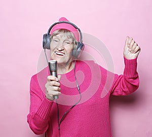 Lifestyle and people concept: Funny old lady listening music with headphones and singing with mic