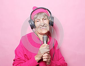 Lifestyle and people concept: Funny old lady listening music with headphones and singing with mic