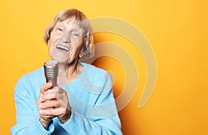 Lifestyle  and people concept: Happy old senior woman singing with microphone, having fun, expressing musical talent