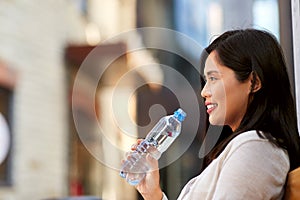 Woman drinking water sitting on wooden city bench