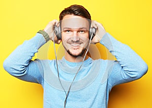 Lifestyle and people concept: Happy young man listening to music with headphones over yellow background