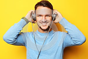 Lifestyle and people concept: Happy young man listening to music with headphones over yellow background