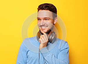 Lifestyle and people concept: Happy young man listening to music with headphones over yellow background